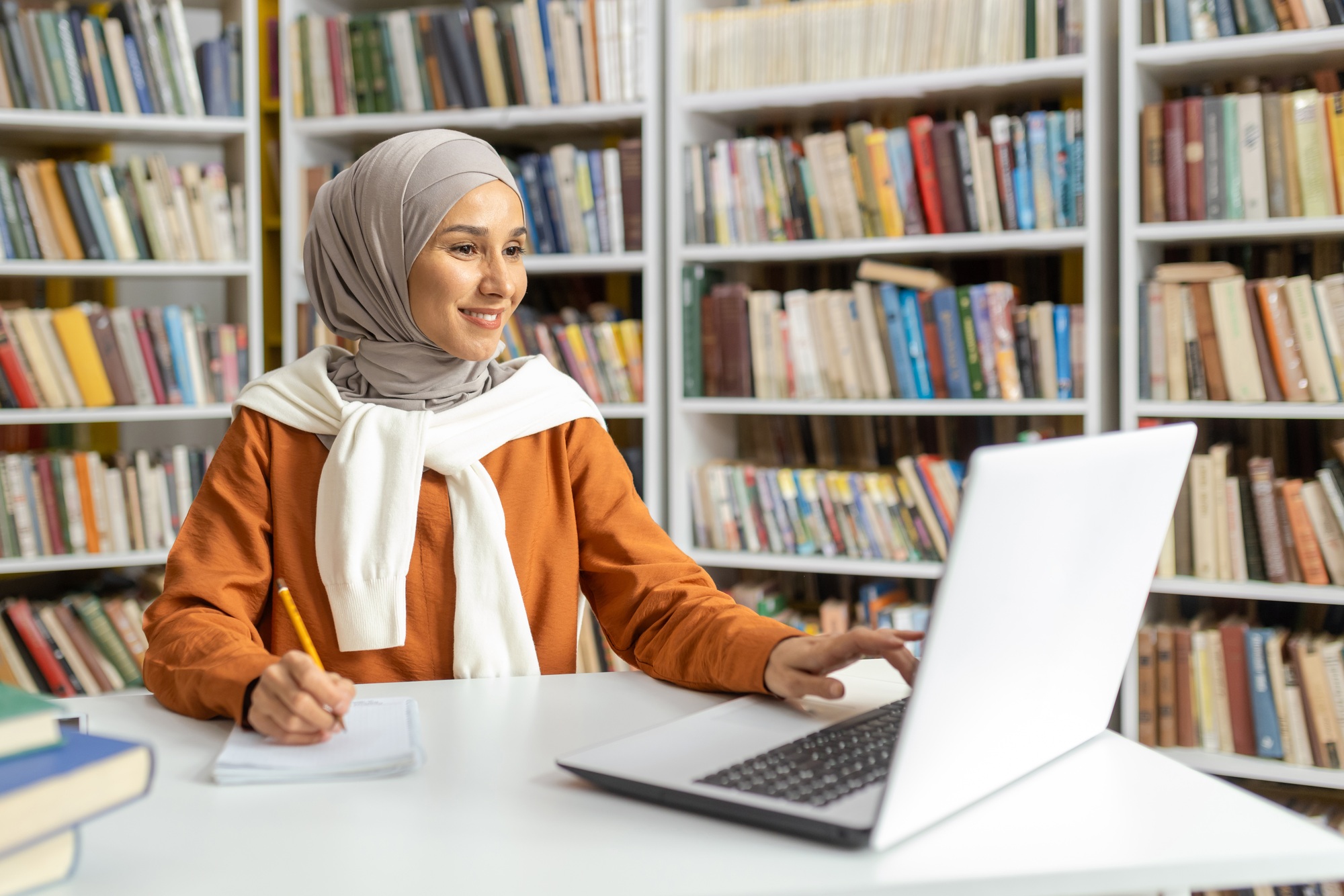 Smiling Muslim woman researching in library with laptop